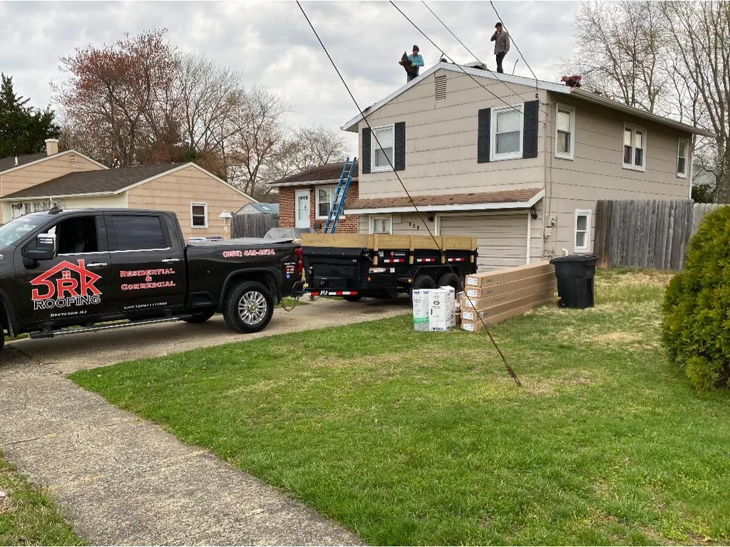 Roofing crew working on a home roof with a company truck and trailer parked at the house