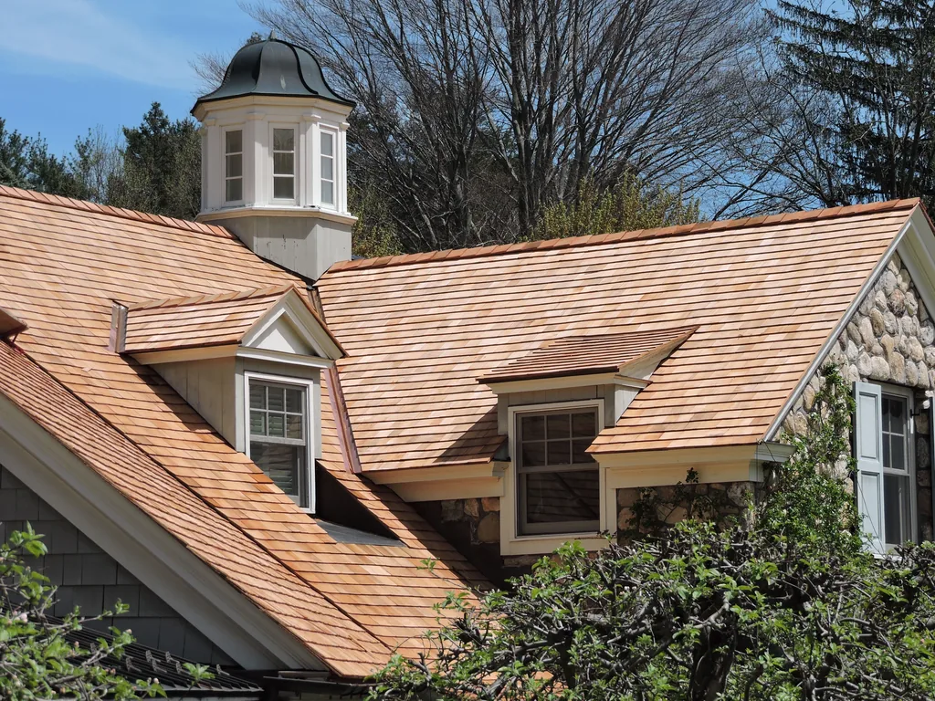 New cedar shake roofing with two dormers and a cupola on a stone and shingle house