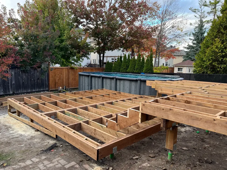 Pressure treated deck framing with joists and beams on posts in a fenced backyard, deck builder