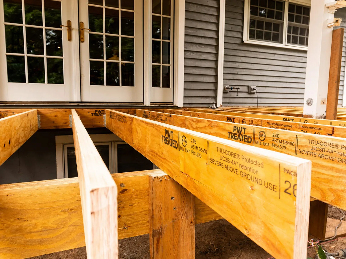 New treated wood deck joists framed against a house, deck builder