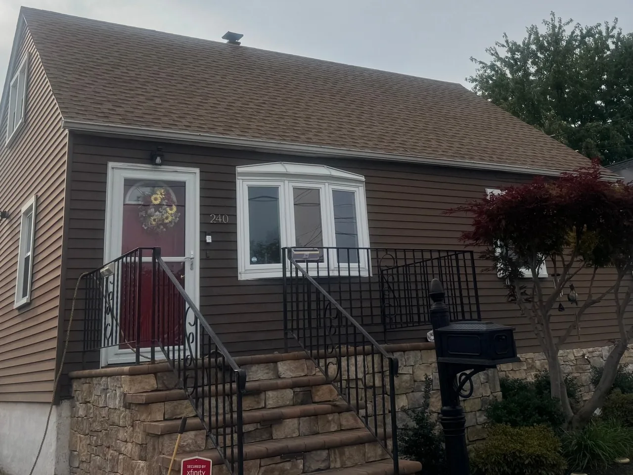 Brown sided cape home with a red entry door and storm door, exterior doors