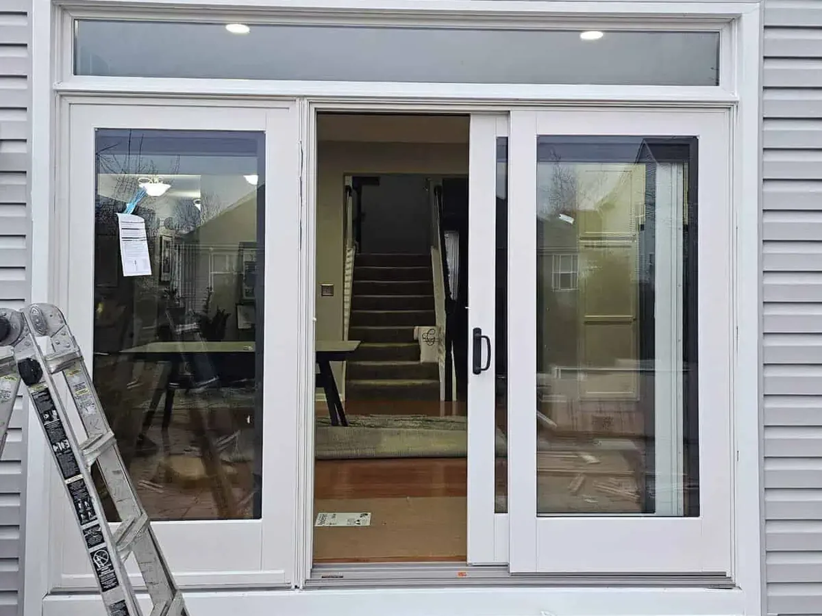 New white sliding glass patio door with a transom window on a gray sided house, exterior doors