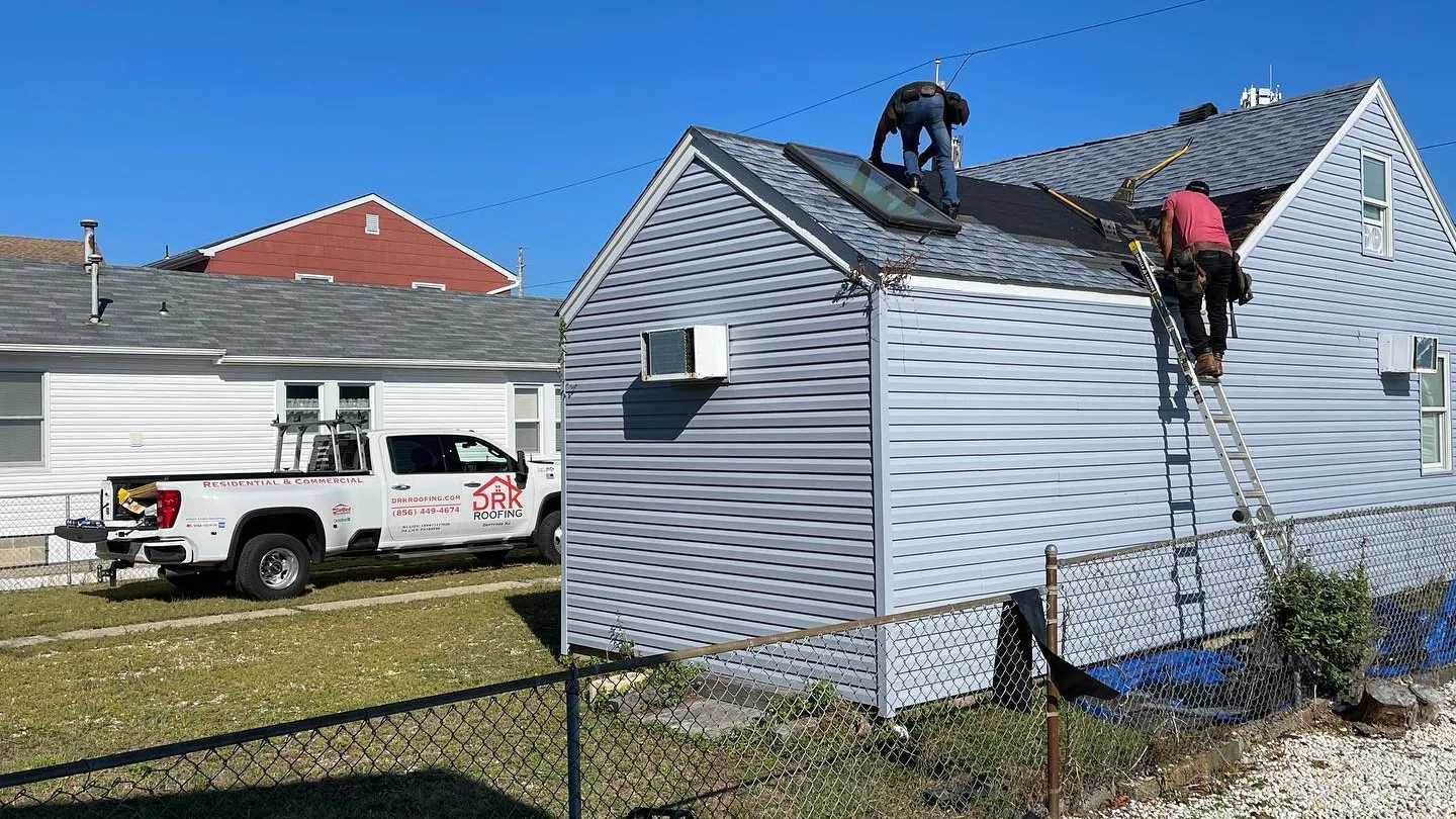 Roofers working on the roof of a gray sided home with a ladder and a work truck