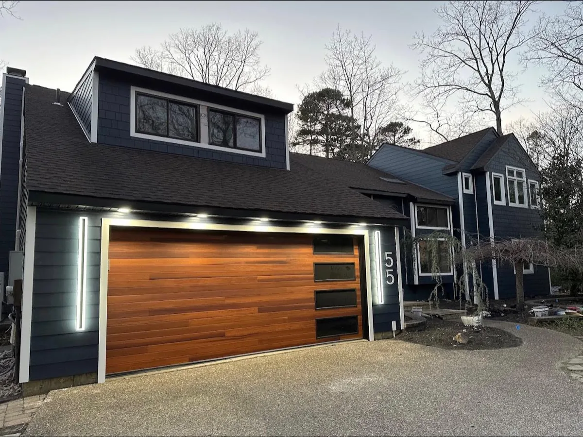 Dark fiber cement siding with a wood look garage door and lit trim on a modern home
