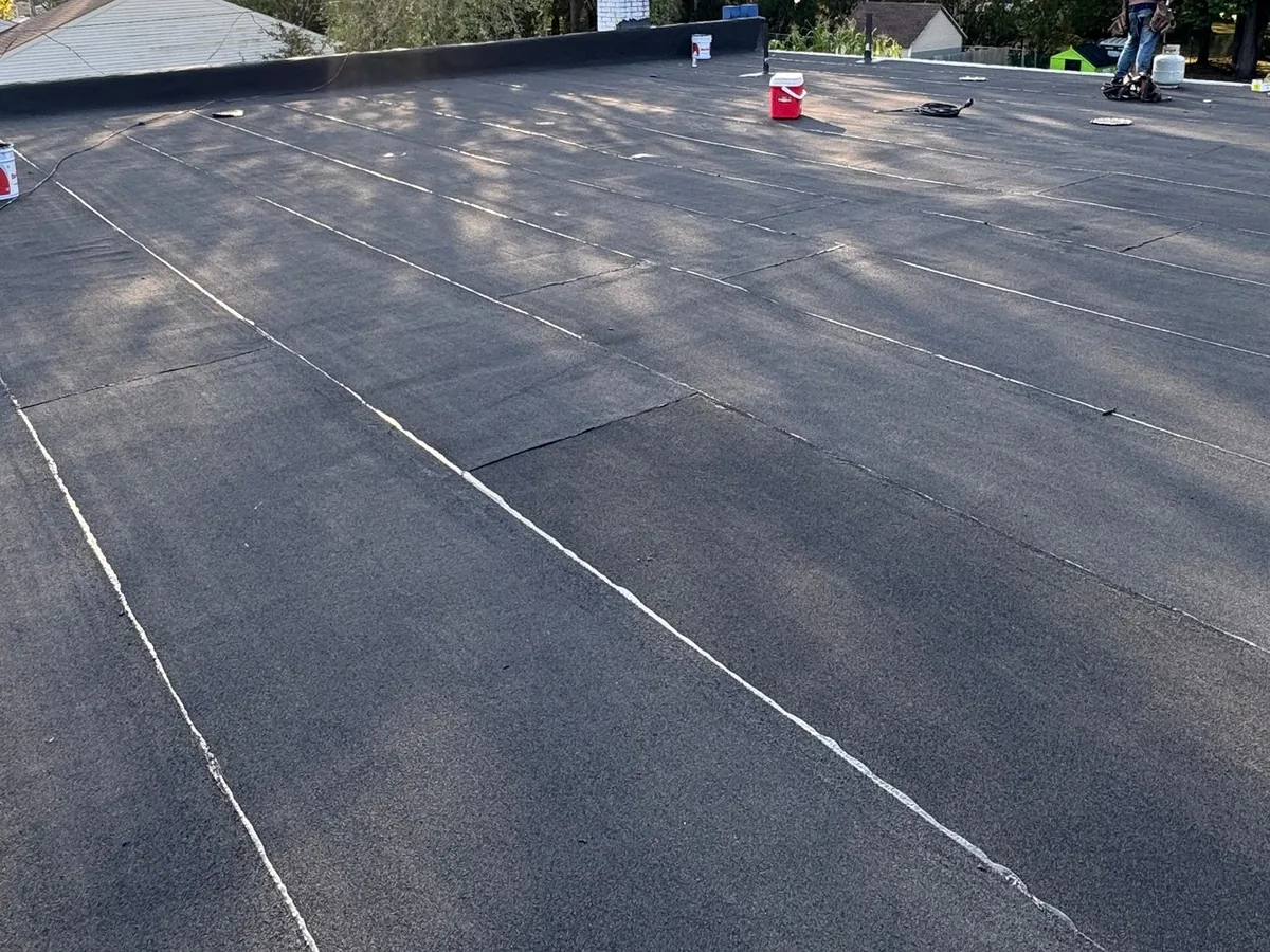 Crew installing a black membrane on a low slope roof, flat roofing
