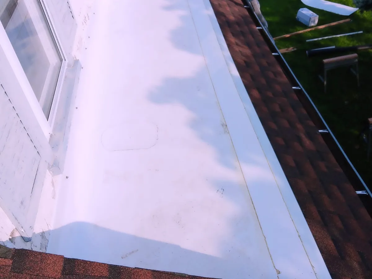 White TPO flat roofing section beside asphalt shingles and metal trim