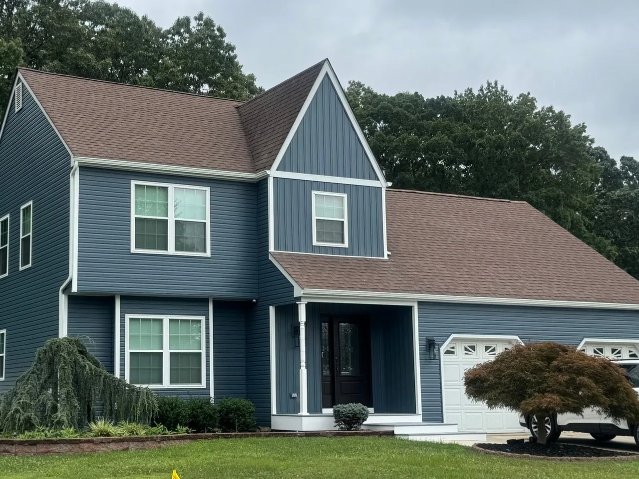 Two story home with new blue lap siding, a board and batten gable and a brown shingle roof, siding