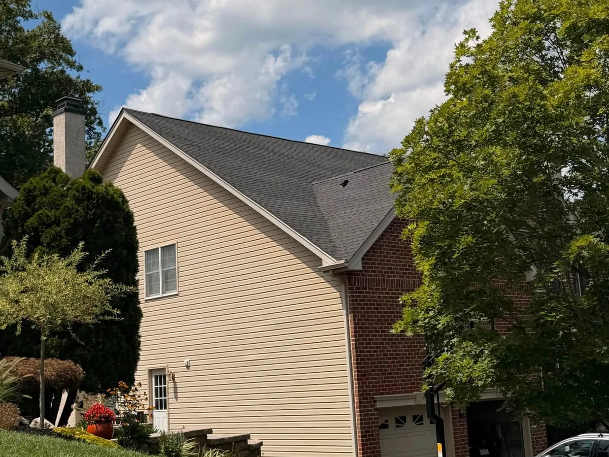 Side view of a new charcoal shingle roof over a tan sided gable and brick garage, roof replacement