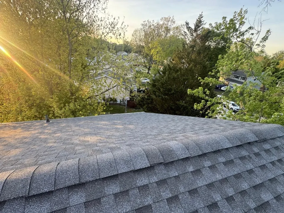 New Pewter Gray asphalt shingles on a roof at sunrise with the neighborhood behind, roof replacement