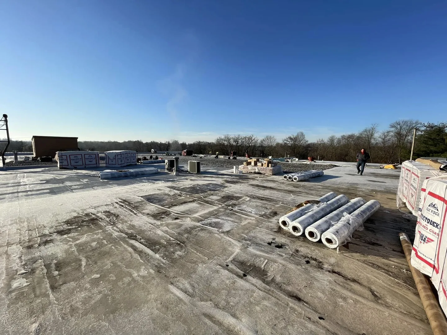 Rolls of flat roofing material and insulation staged on a large commercial roof, commercial roofing