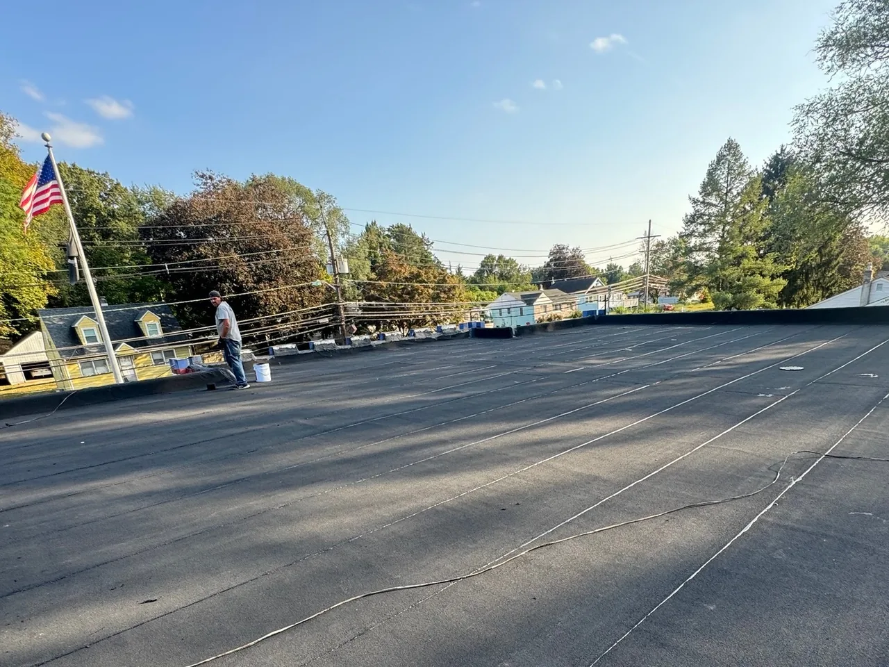 Crew member on a new black flat roofing membrane with an American flag beyond, flat roofing