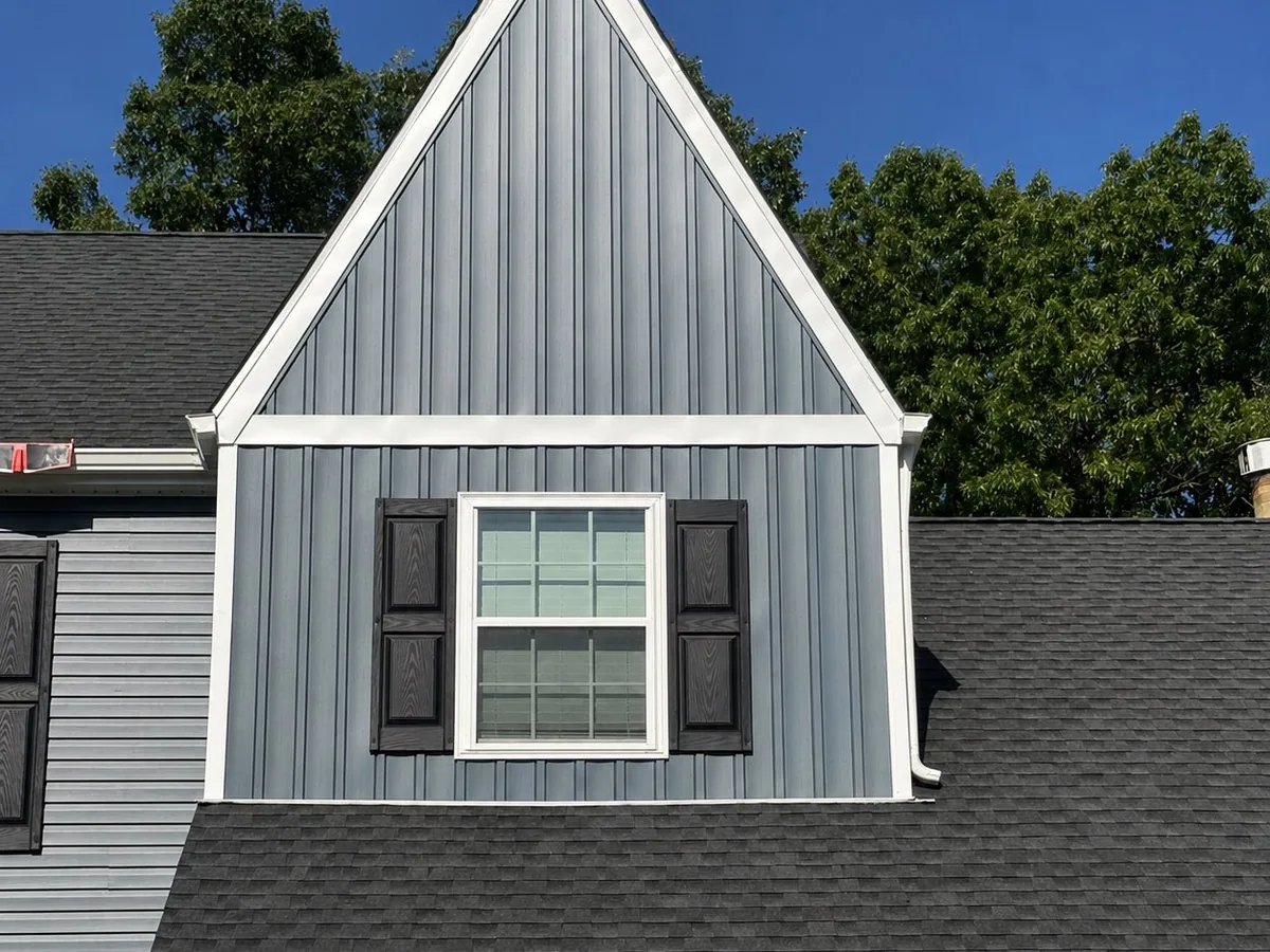 Gray board and batten gable with a shuttered window above a new asphalt shingle roof, siding and roofing