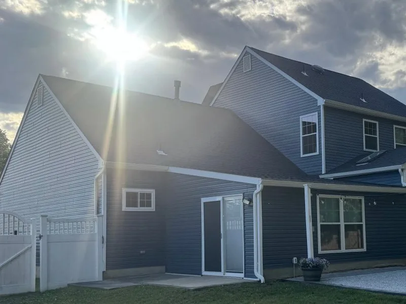 Rear of a blue sided two story home under a new asphalt shingle roof, roof replacement
