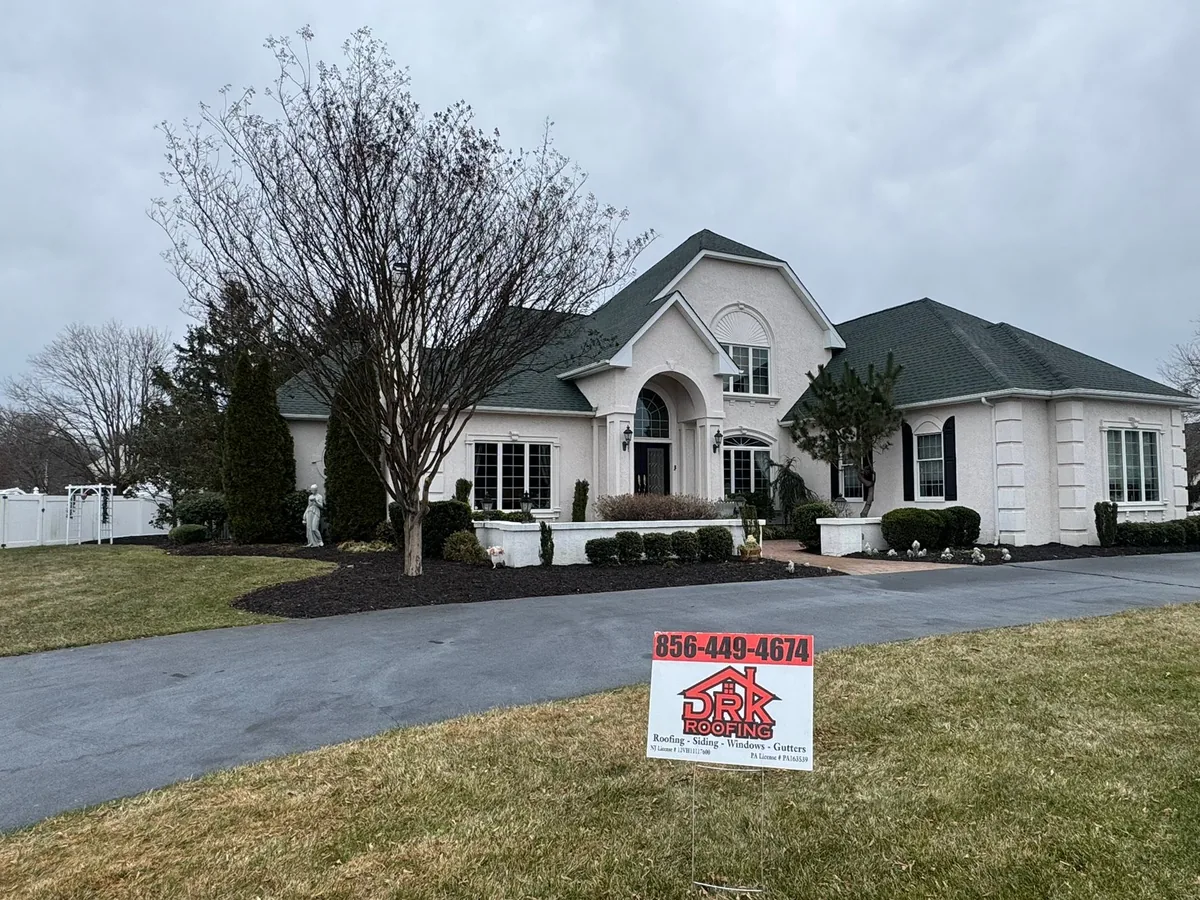 Stucco home with a new green shingle roof and a company yard sign in the lawn, roof replacement