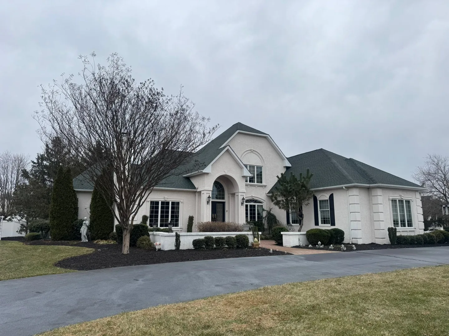 Stucco home with arched windows under a new Hunter Green asphalt shingle roof, roof replacement