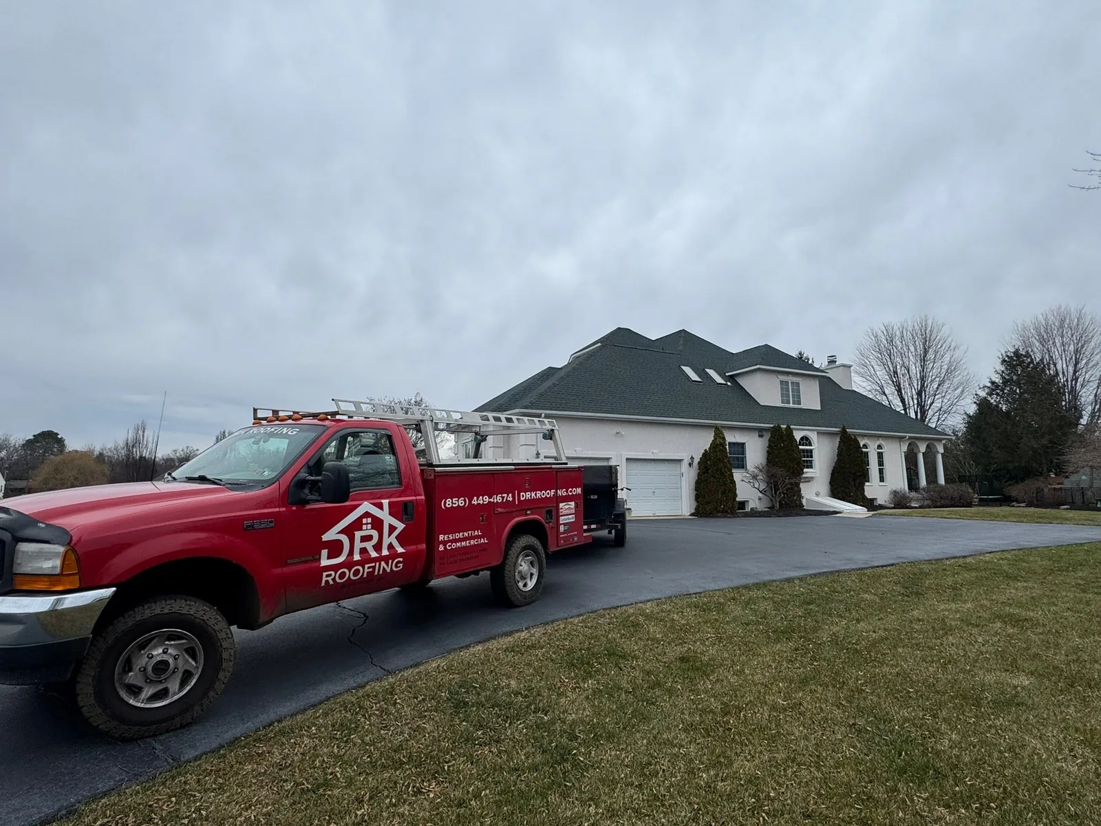 Red company pickup in the driveway of a stucco home with a new green shingle roof, roof replacement