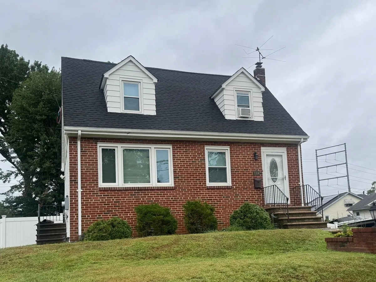 Brick cape with two dormers under a new dark asphalt shingle roof, roof replacement