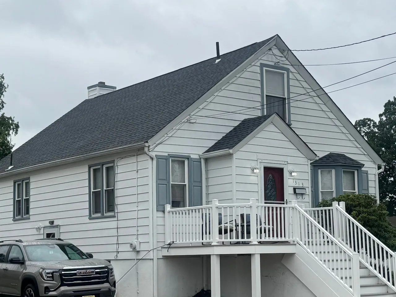 Rear of a white cape with a new dark asphalt shingle roof and a white deck, roof replacement