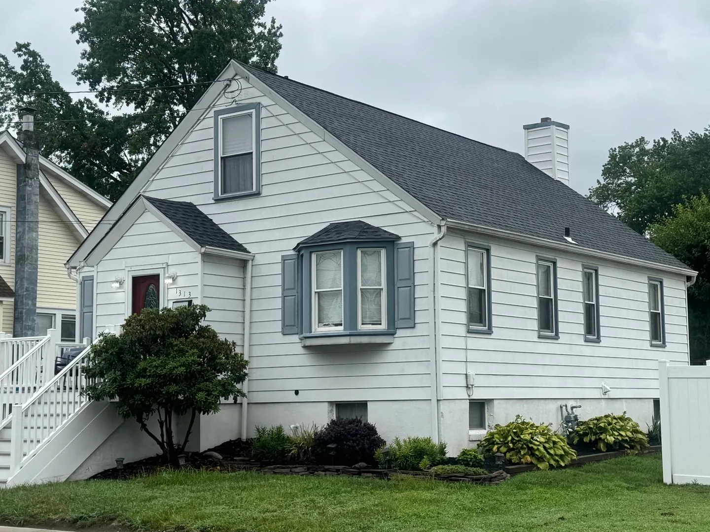 White cape with blue shutters and a new dark asphalt shingle roof, roof replacement