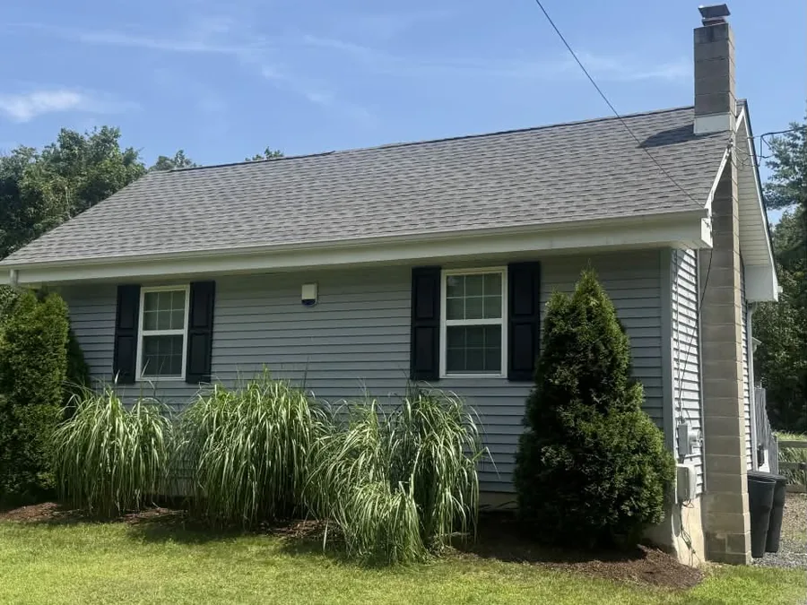 New asphalt shingle roof beside a stone chimney on a gray sided ranch, roof replacement