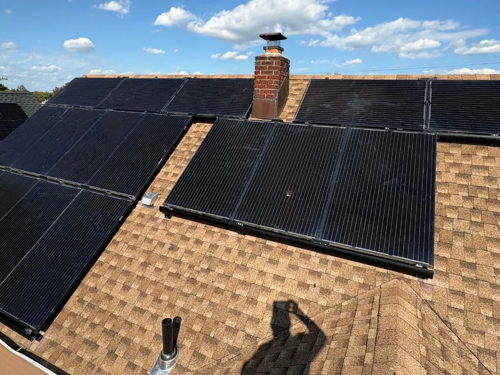 Black solar panels reinstalled on a new brown asphalt shingle roof beside a brick chimney, roof replacement