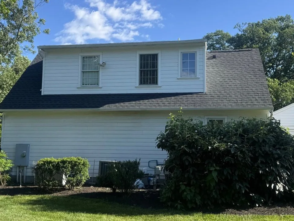 Rear dormer and garage wing of a white colonial under a new asphalt shingle roof, roof replacement