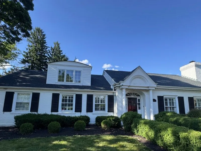 White brick colonial with black shutters under a new dark asphalt shingle roof, roof replacement