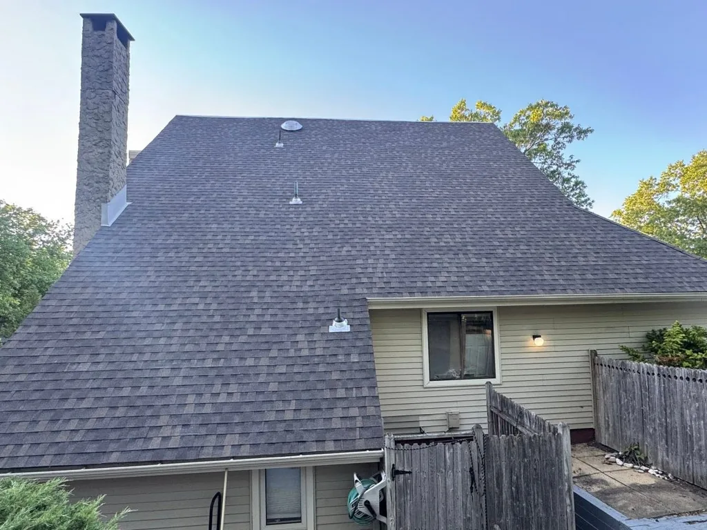 Rear roof slope with new asphalt shingles beside a stone chimney, roof replacement