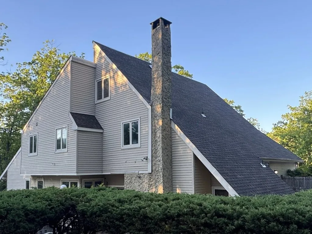 Contemporary home with a stone chimney and a new dark asphalt shingle roof, roof replacement