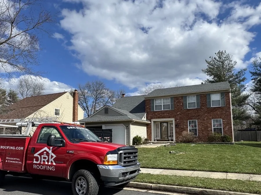 Red company pickup parked at a brick colonial with a new Pewter Gray shingle roof, roof replacement
