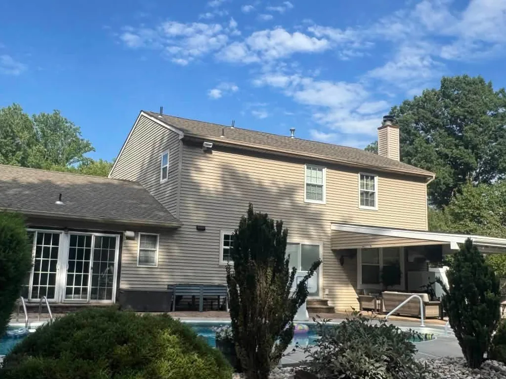 Rear of a tan sided colonial with a new asphalt shingle roof over the house and patio cover, roof replacement