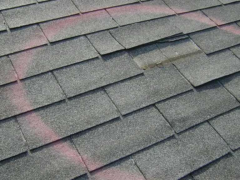 Damaged asphalt shingle circled in paint during a roof repair inspection