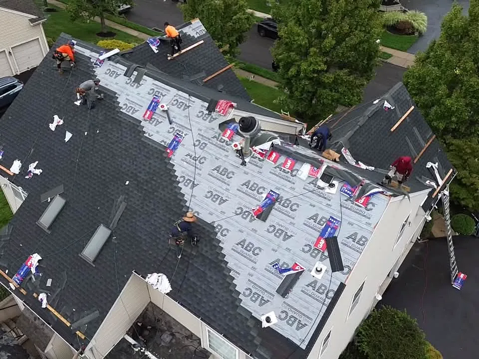 Aerial view of a crew laying underlayment during a roof replacement on a two story home
