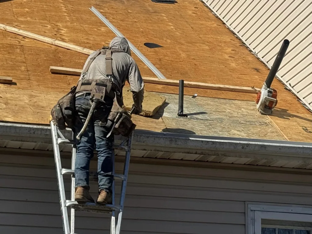 Roofer on a ladder at the edge of a stripped roof deck during a roof replacement
