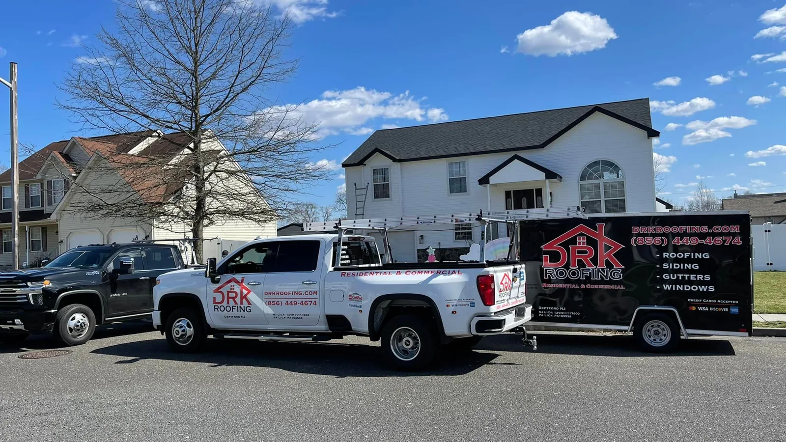 Roofing and siding company trucks and a work trailer parked on a residential street