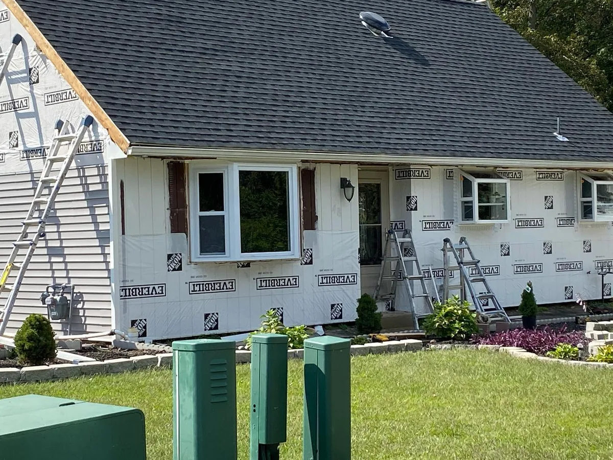 House wrap and ladders on a cape home during new siding installation, siding contractor