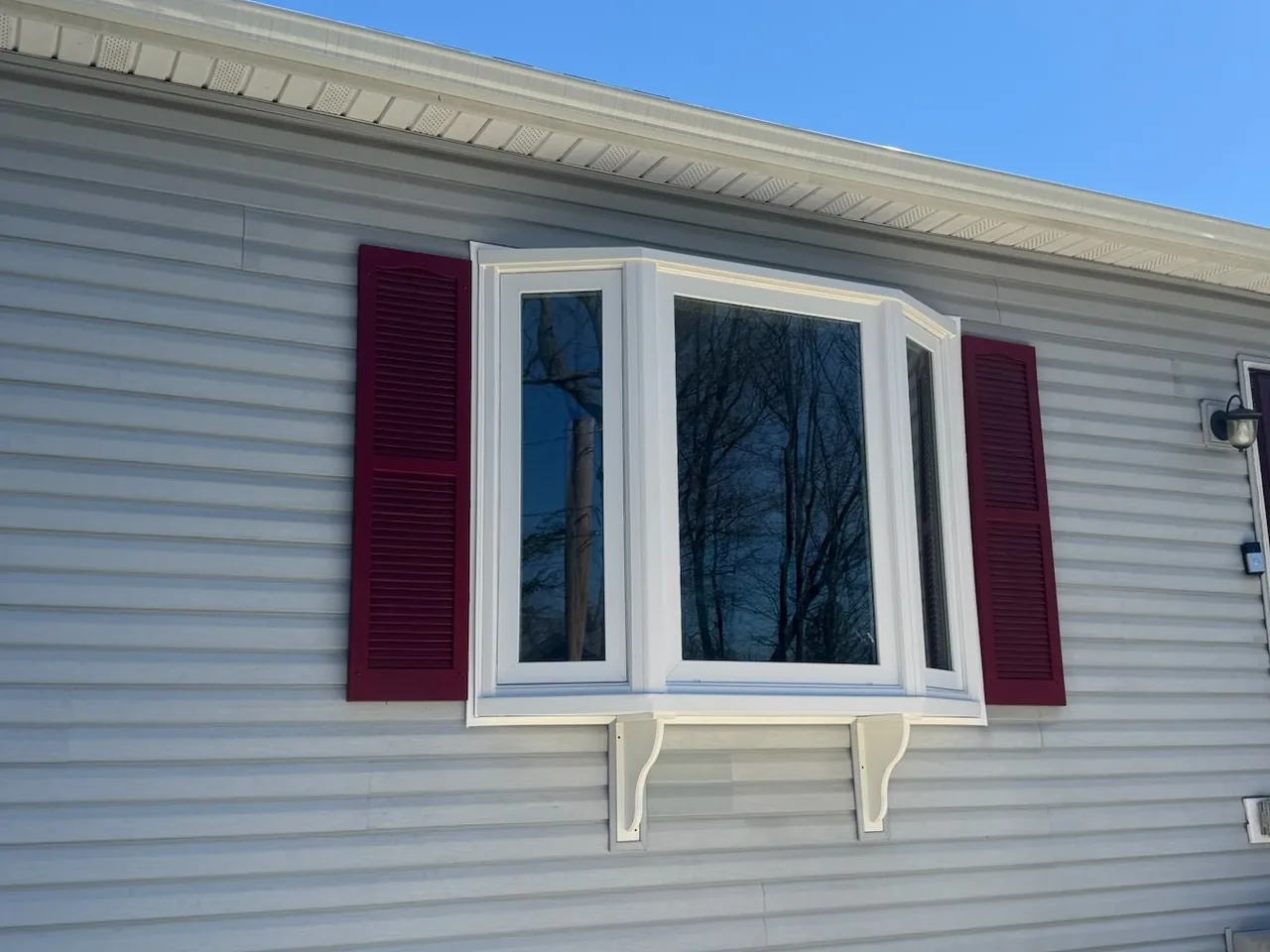 New bay window with red shutters set in gray vinyl siding, window replacement